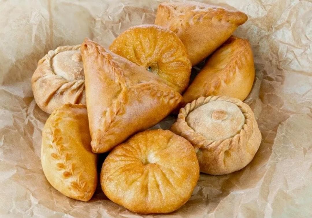 Печёные пирожки и самса с плетёными краями на пекарской бумаге